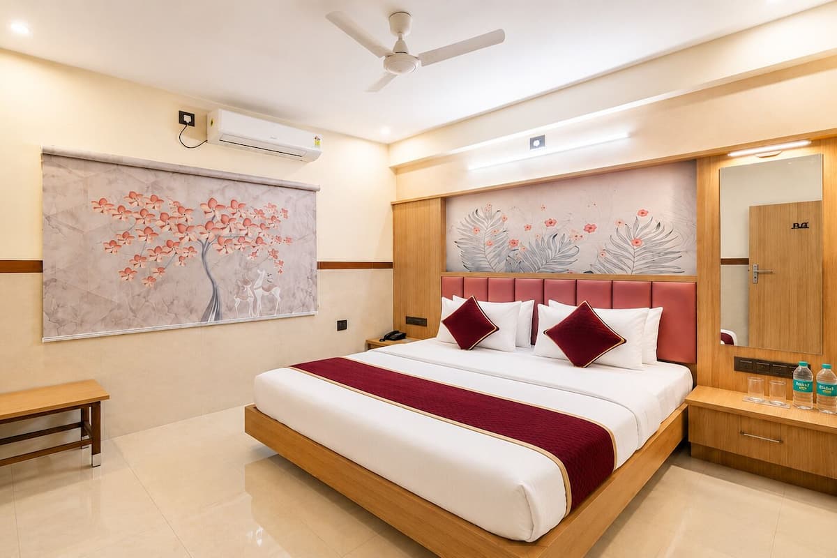 A hotel room with a bed, a bench, a bedside table with a mirror, and a wall-mounted air conditioner.