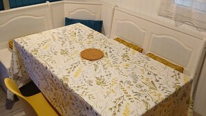 A room with a white bed, a table with a floral tablecloth, and yellow chairs.