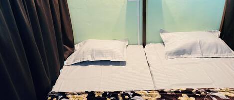 Un lit double avec du linge de lit blanc, une couvre-lit à motifs floraux et un mur vert clair doté de deux prises électriques.
