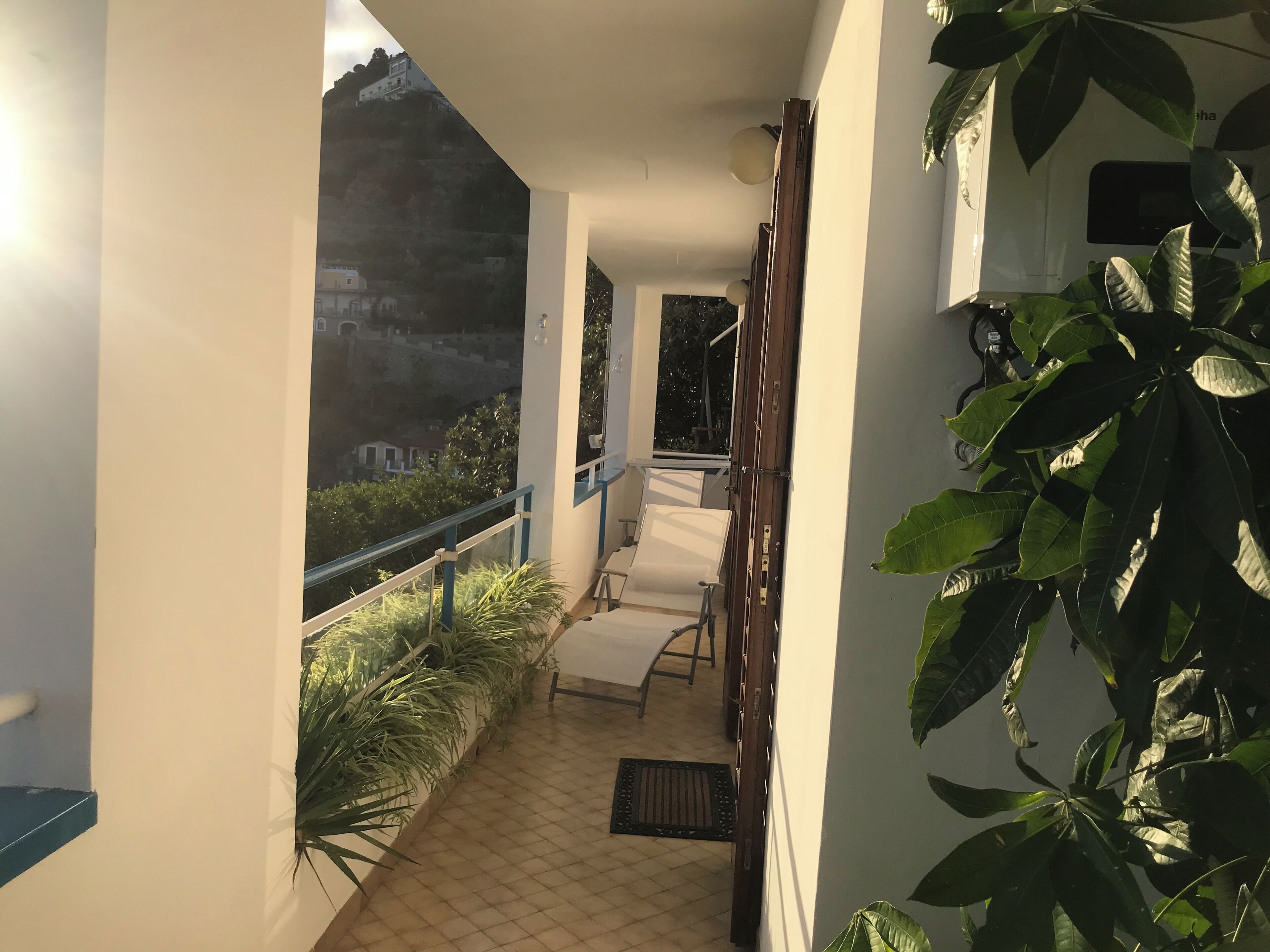 Un balcón con vistas a una colina, una silla y plantas en macetas.