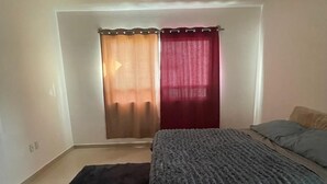 Un dormitori amb un llit, una catifa fosca i una finestra amb cortines.