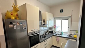 A modern kitchen with stainless steel appliances, a white fridge, and a yellow decorative item on top. - 2 Bedroom Apartment Marconi Trastevere Station (Roma)