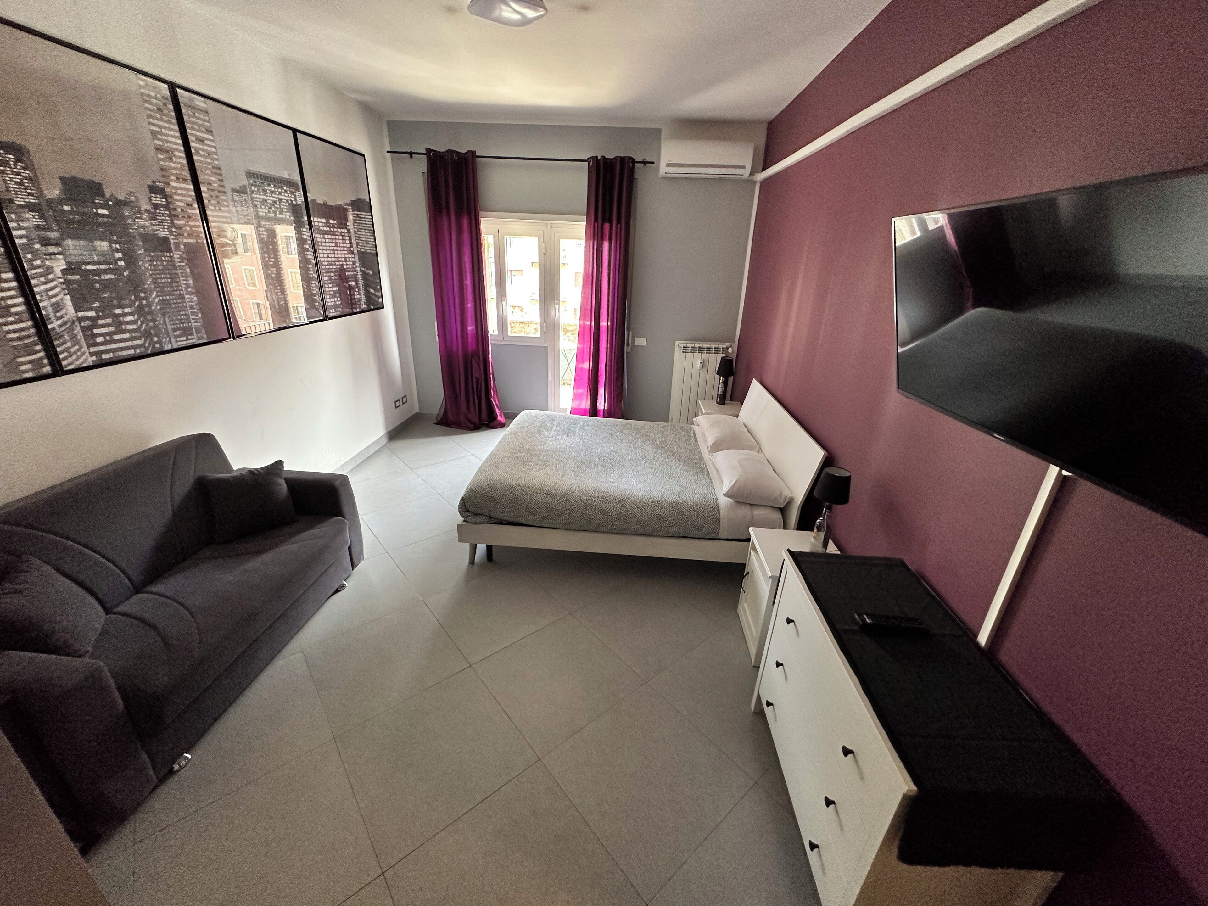 Una camera da letto moderna con un letto, un divano, una TV e vista sulla città.