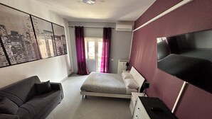 A modern bedroom with a bed, a sofa, a TV, and a cityscape view. - 2 Bedroom Apartment Marconi Trastevere Station (Roma)