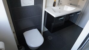 A modern bathroom with a toilet, sink, and dark tiled walls. - 2 Bedroom Apartment Marconi Trastevere Station (Roma)