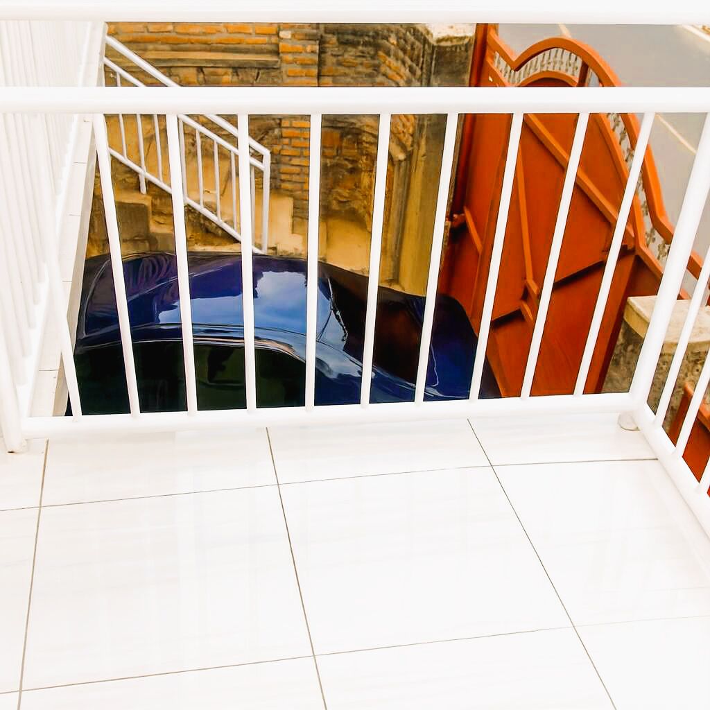 A white balcony railing overlooking a blue car and an orange structure.