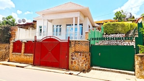 A two-story house with a red gate and a green gate, a white balcony, and a stone wall. - Parkviewperch (Kigali)