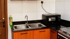 A compact kitchen with wooden cabinets, a black microwave, and a stainless steel sink. - Parkviewperch (Kigali)