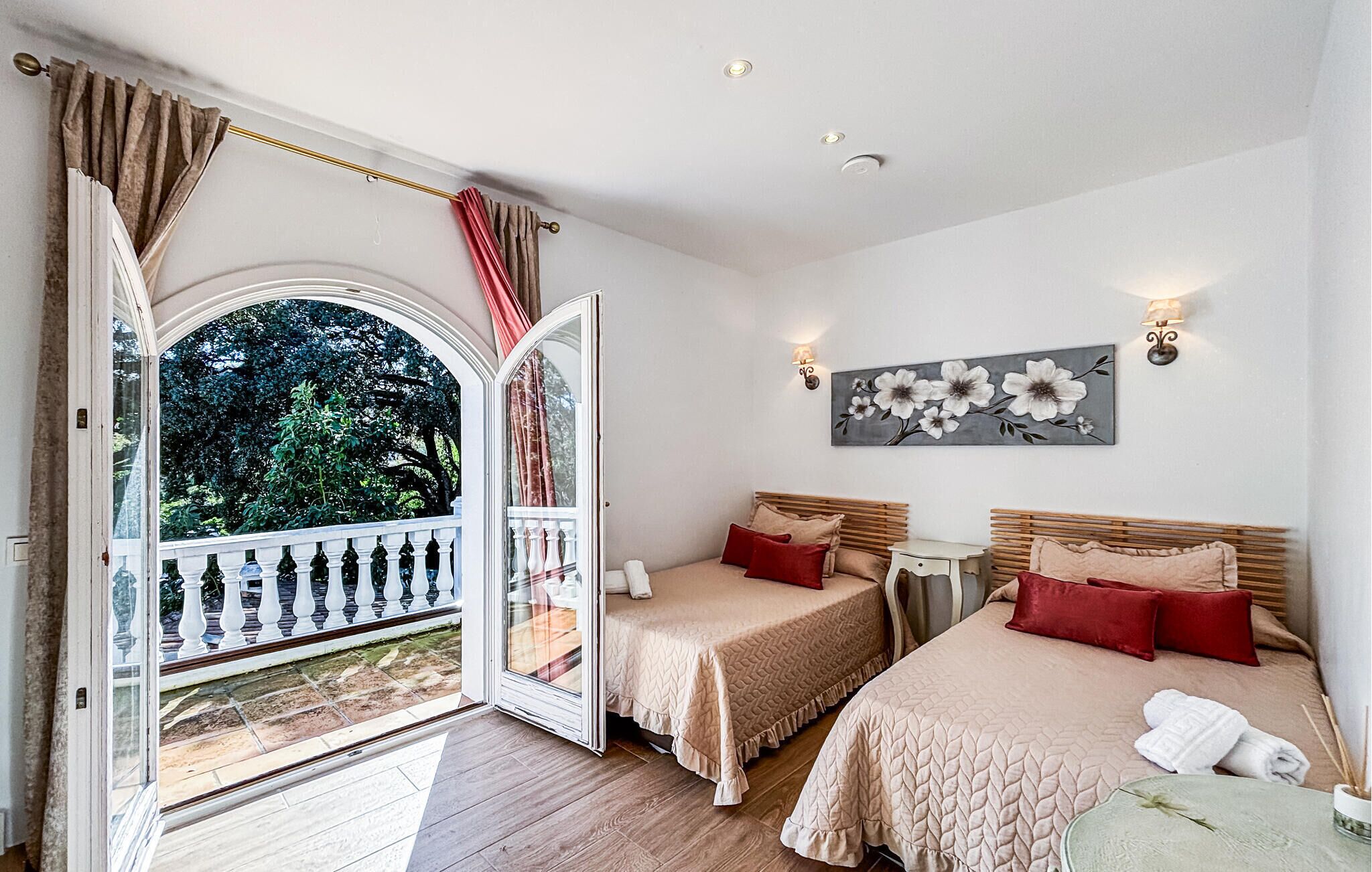 A bedroom with two beds, a balcony, and a view of greenery.