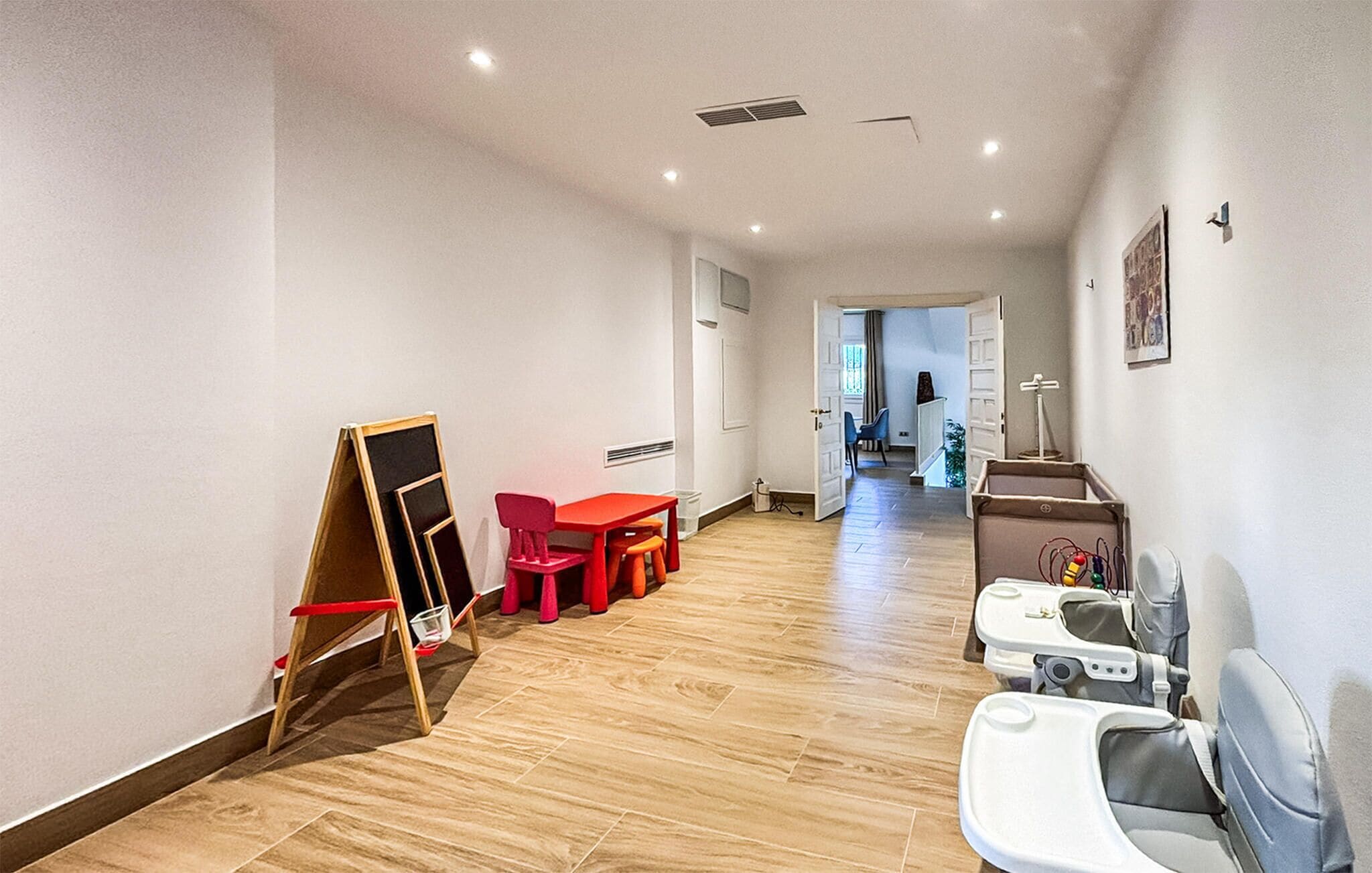 A hallway with a red table and stools, a whiteboard, and a baby changing station.