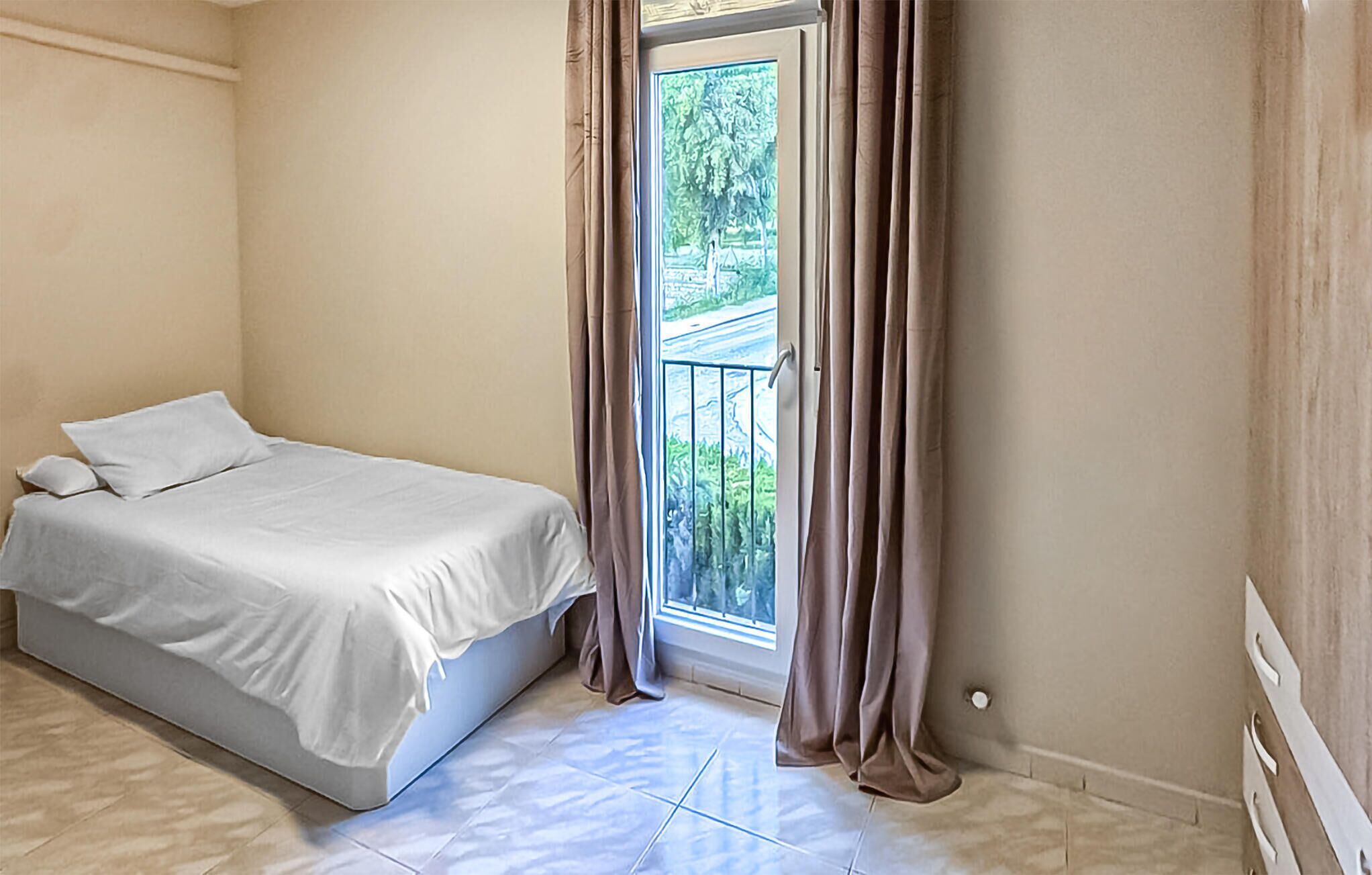 Un dormitorio con cama, ventana con cortinas y vista a la vegetación exterior.