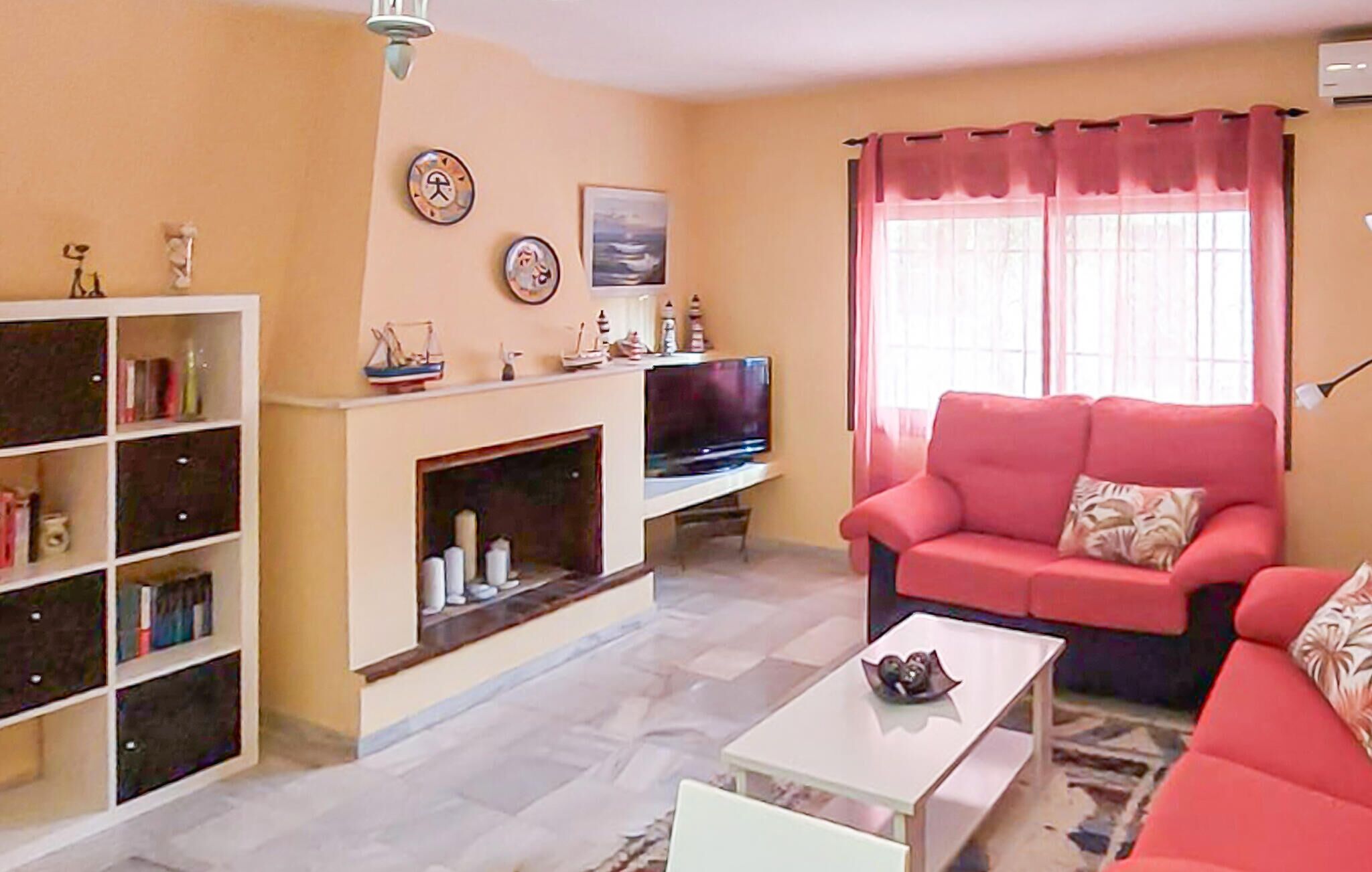 Una sala de estar con chimenea, un sofá, un televisor y una estantería.