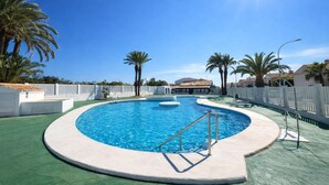 Ein kreisförmiger Pool mit Sprungbrett, umgeben von Palmen und einem weißen Zaun.