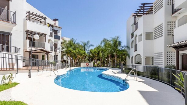 Piscina rodeada por uma cerca branca, com um céu azul límpido acima.
