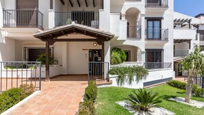 Um edifício residencial com vários andares, varandas, um alpendre coberto e um jardim bem cuidado.
