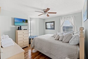 Una camera da letto con un letto, una ventola a soffitto, una TV, una cassettiera e una finestra con tende.