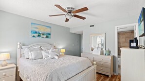 Une chambre à coucher comprenant un lit, des tables de chevet, une commode, un ventilateur de plafond, un tableau et un miroir.