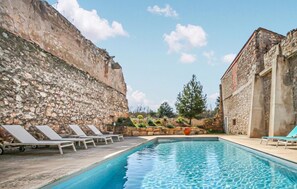 Uma piscina com espreguiçadeiras, uma parede de pedra e um edifício com arquitetura em pedra.