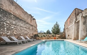 A swimming pool with lounge chairs, a stone wall, and a building with a stone facade. - Maison piscine proche mer (Portel Des Corbieres)