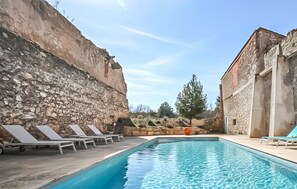 A swimming pool with lounge chairs, a stone wall, and a building with stone facade. - Maison piscine proche mer (Portel Des Corbieres)