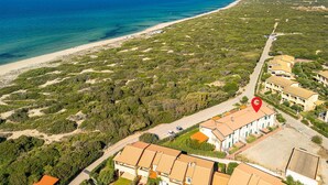 Ett flygbildsbild av ett kustområde med en strand, tät vegetation och en rad byggnader. En röd markör visar en specifik plats.