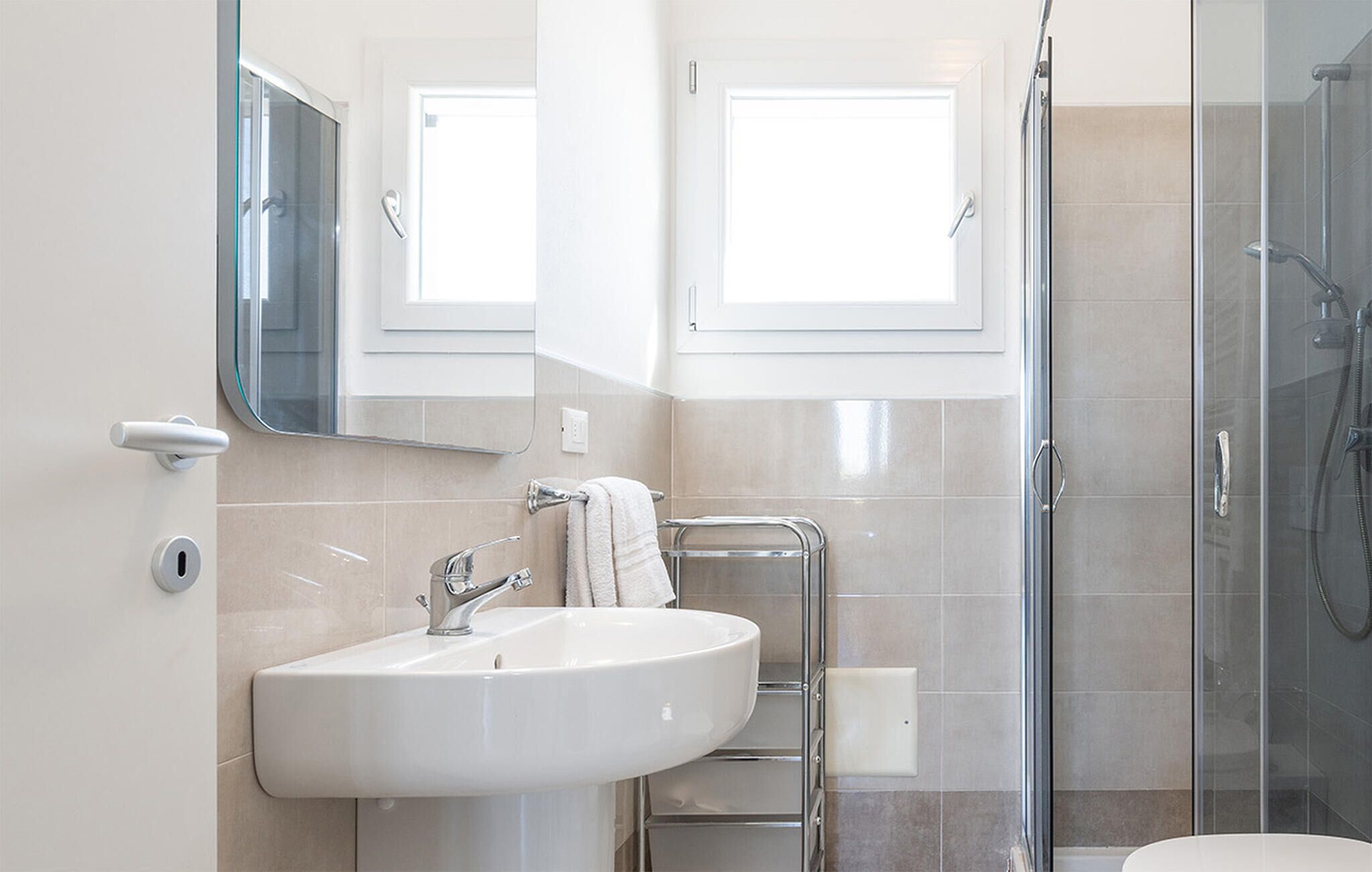 Ein modernes Badezimmer mit Waschbecken, Spiegel, Handtuchhalter und Duschkabine aus Glas.