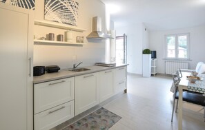 Eine moderne Küche mit weißen Schränken, einer Edelstahlspüle und einem eingebauten Herd. Ein Fenster sorgt für natürliches Licht und einen Ausblick ins Freie.
