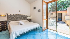 Une chambre à coucher comprenant un lit, une commode, une table de chevet et une grande porte-fenêtre coulissante donnant sur un espace extérieur.