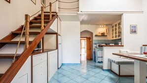 Une cuisine spacieuse avec des carreaux bleus, un escalier en bois et un coin repas agrémenté d’une nappe à rayures.