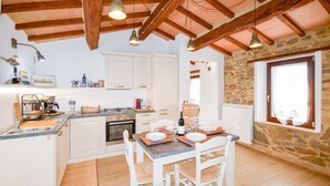 Una cocina con armarios blancos, una mesa de comedor para cuatro personas y una pared de piedra con ventana.