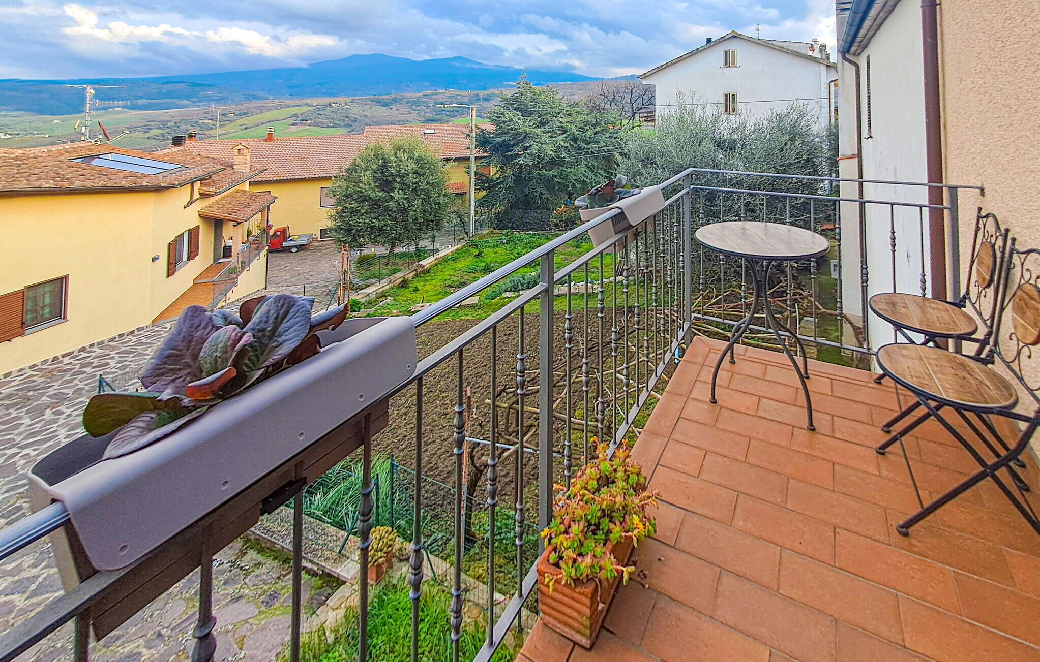 A balcony with a view of a rural landscape, a table with chairs, and a potted plant.