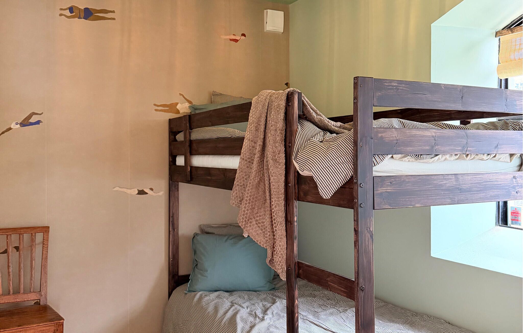 A bunk bed room with a wooden headboard, a window with a view, and a small wooden bench.