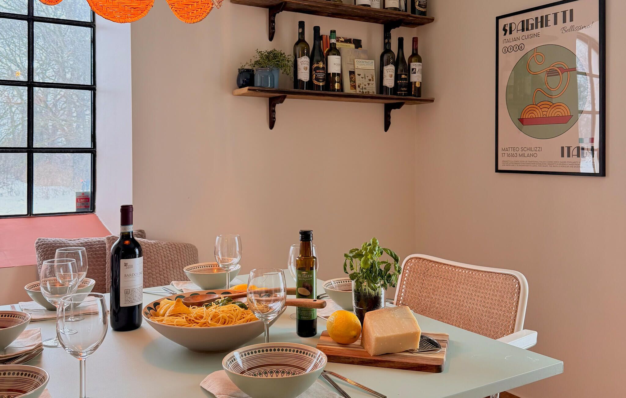 Une table à manger avec un plat de spaghettis, une bouteille de vin, des verres et un morceau de fromage.