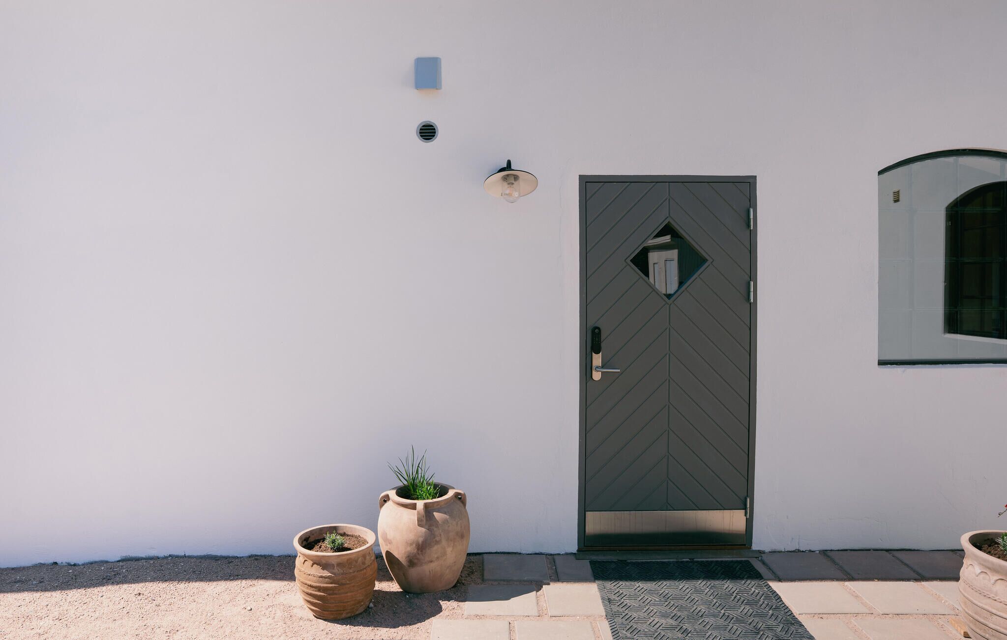 Un bâtiment moderne avec une porte sombre, une petite fenêtre et deux grands pots contenant des plantes.