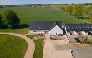 A large, modern farmhouse with a spacious driveway, a well-maintained lawn, and a view of surrounding fields.
