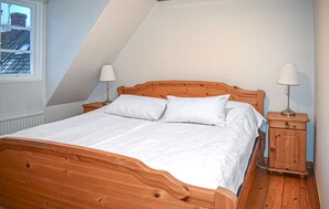 A bedroom with a wooden bed, white bedding, two bedside tables with lamps, and a view of the outside through a window. - 3 bedroom nice home in Simrishamn (Simrishamn)