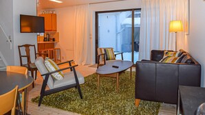 A modern living room with a sofa, chairs, a small table, a TV, and a kitchen area. - 3 bedroom nice home in Simrishamn (Simrishamn)