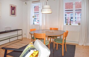 A dining area with a round table, six chairs, a hanging light fixture, and a view of a red-roofed building through a window. - 3 bedroom nice home in Simrishamn (Simrishamn)
