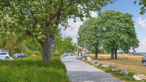 A paved pathway flanked by lush greenery and trees, with a blue sign indicating a parking area. - 3 bedroom nice home in Simrishamn (Simrishamn)