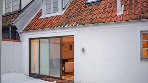 A white building with a red-tiled roof, a sliding glass door leading to an interior with a visible chair and table, and a small window on the upper floor. - 3 bedroom nice home in Simrishamn (Simrishamn)