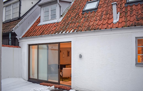 A white building with a red-tiled roof, a sliding glass door leading to an interior with a visible chair and table, and a small window on the upper floor.