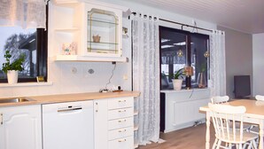 Moderni keittiö, jossa on valkoiset kaapit, puinen työtaso sekä ruokailutila, jossa on valkoinen pöytä ja tuolit.
