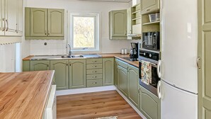 Eine Küche mit grünen Schränken, einer Holz Arbeitsplatte, einer Spüle, einer Kaffeemaschine, einem Backofen und einem Kühlschrank.