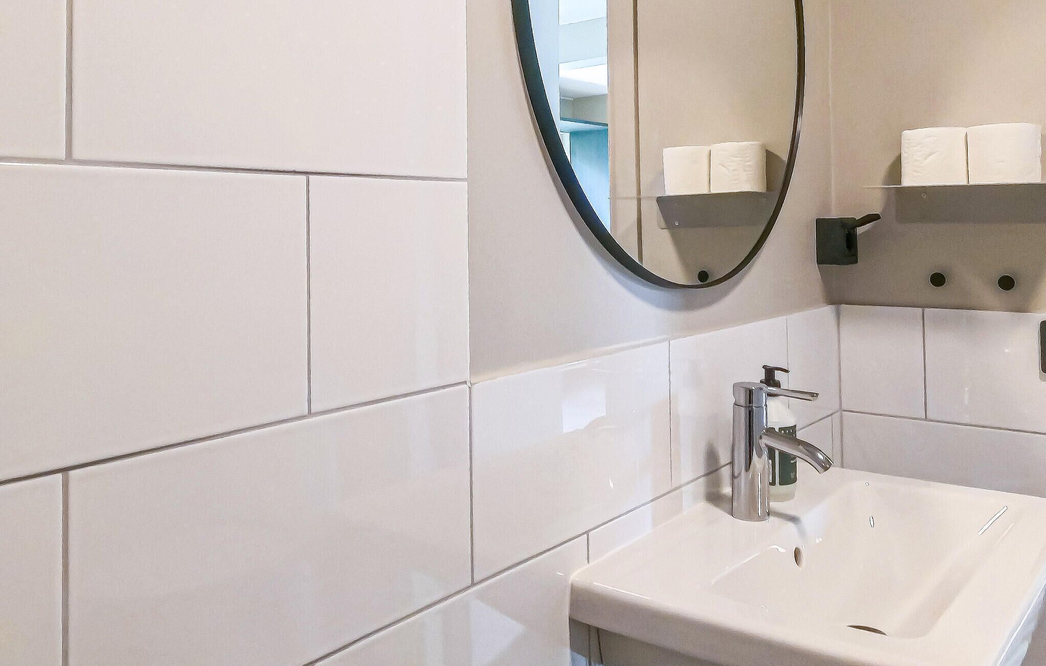 Une salle de bain avec des carreaux blancs, un lavabo, un miroir et un porte-rouleau de papier toilette.