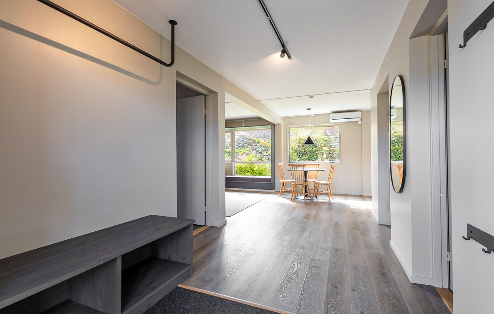 A modern interior with a wooden floor, a bench, a dining area with chairs, and a large window.