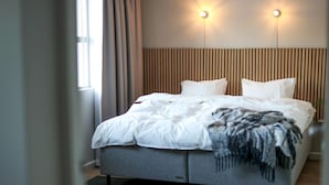A modern hotel room with a large bed, two bedside tables, a wooden slatted headboard, and two wall-mounted lights. - Lovely apartment in Myggenäs (Myggenäs)