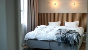 A modern hotel room with a large bed, two bedside tables, a wooden slatted headboard, and two wall-mounted lights. - Apartment in Myggenäs (54703) (Myggenäs)