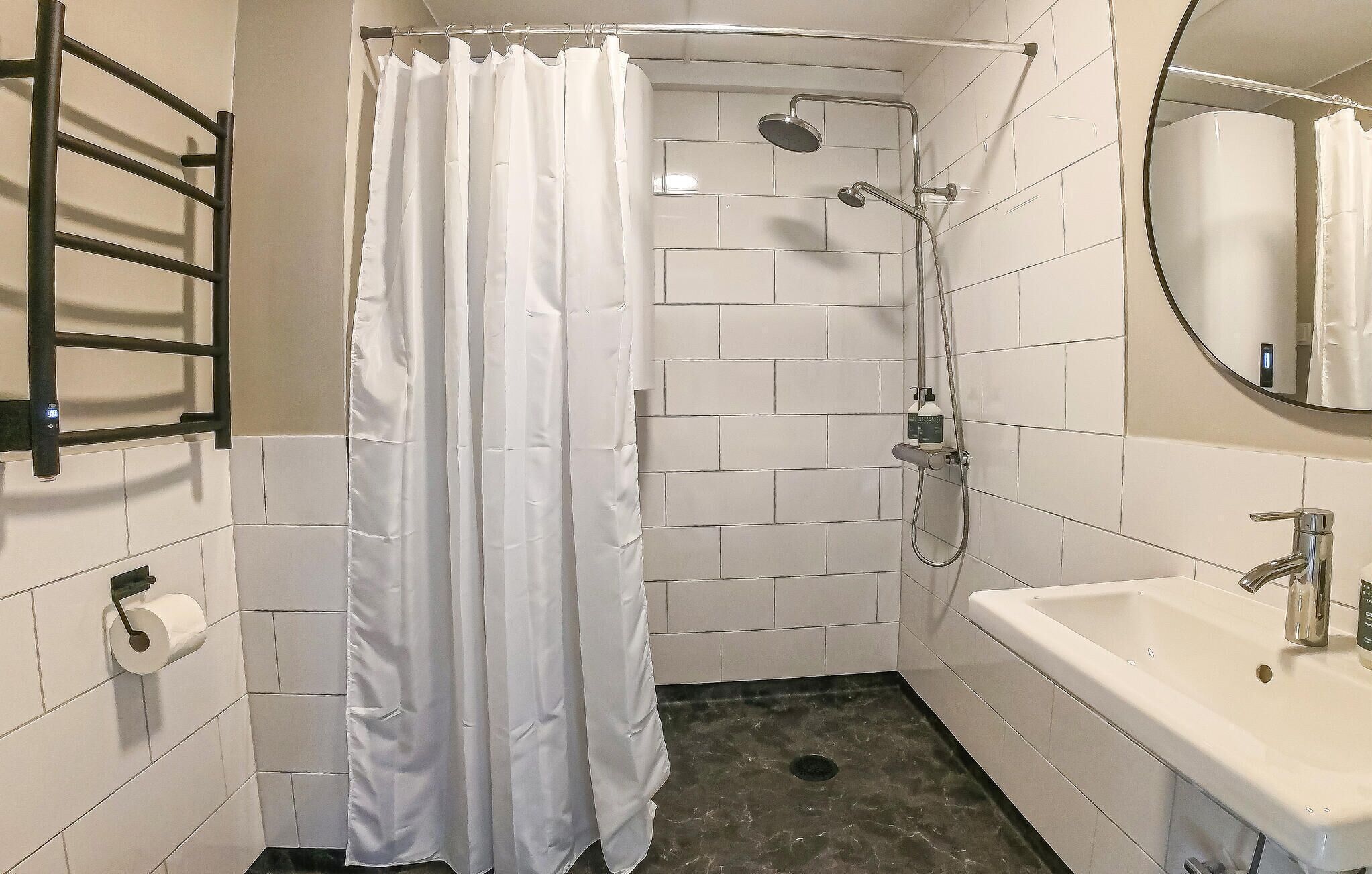 A bathroom with a shower, toilet paper, a towel rack, a sink, and a mirror.