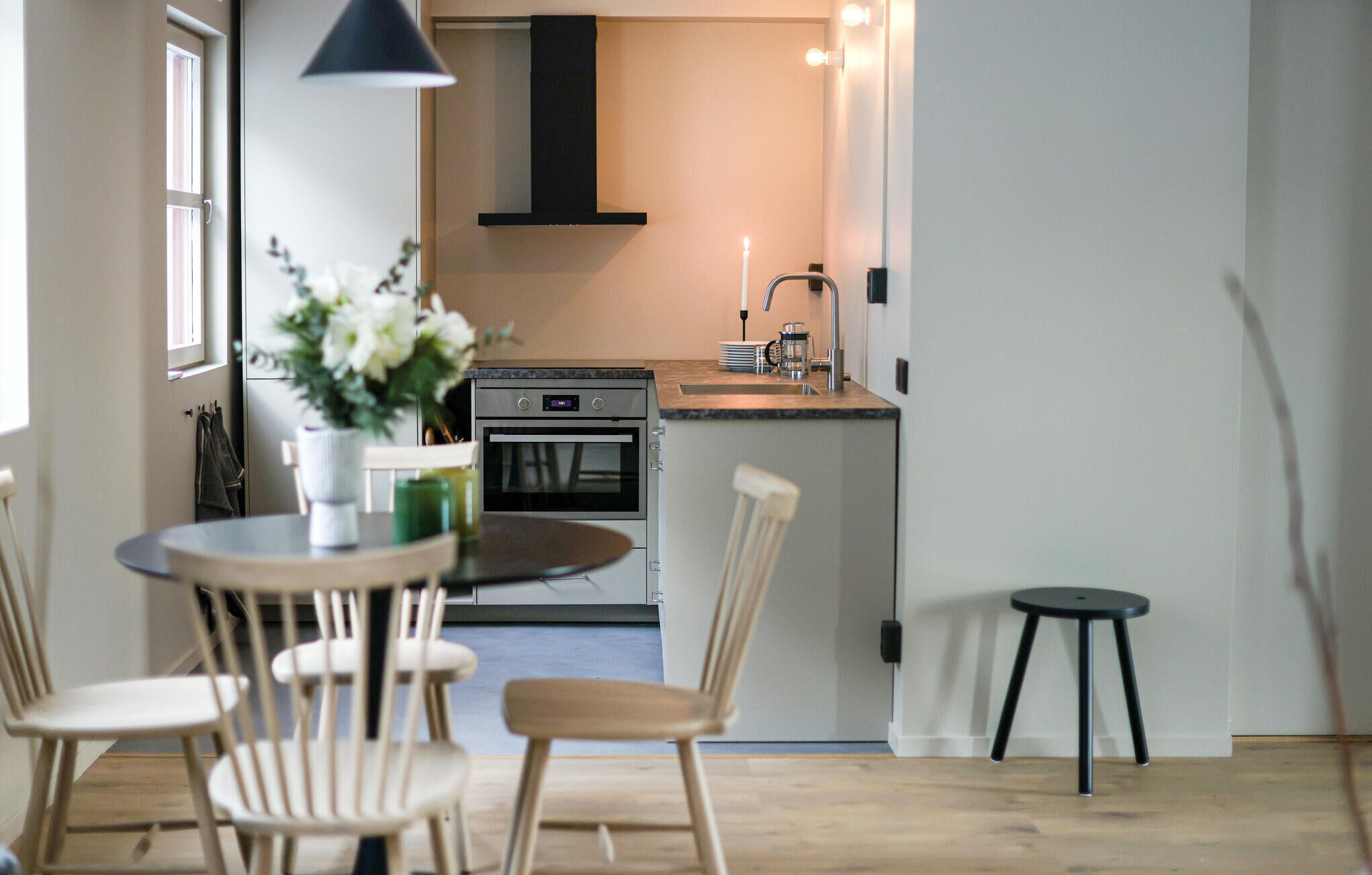 A modern kitchen with a built-in oven, a sink, and a dining area with a round table and chairs.