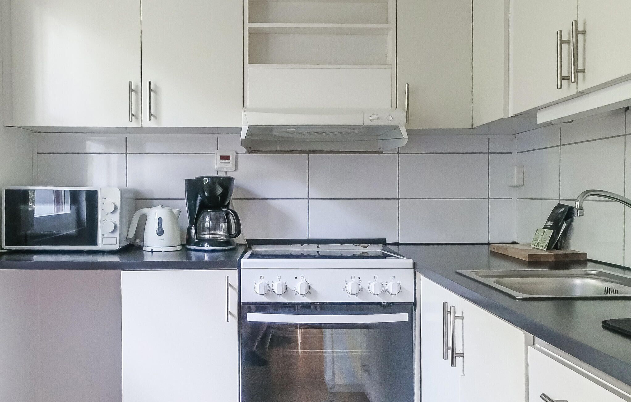 A kitchen with white cabinets, a microwave, a coffee maker, and a stove.